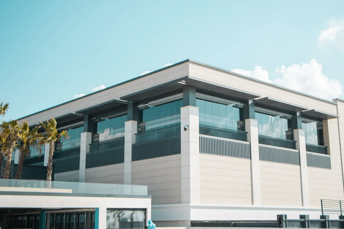 A modern commercial building with a glass upper floor and palm trees at the entrance